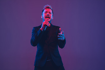 Image showing Young caucasian musician, performer singing, dancing in neon light on gradient background