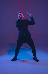 Image showing Young caucasian musician, performer singing, dancing in neon light on gradient background