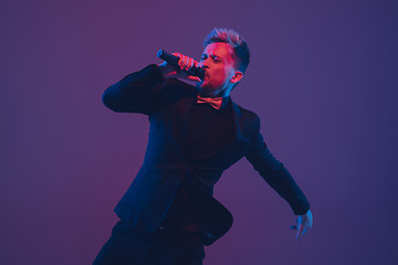 Image showing Young caucasian musician, performer singing, dancing in neon light on gradient background