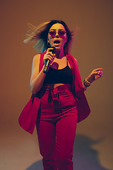 Image showing Young caucasian female musician, performer singing, dancing in neon light on gradient background