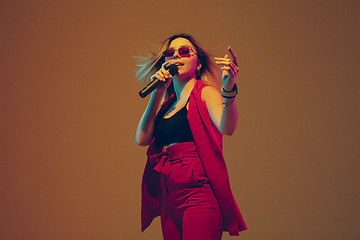 Image showing Young caucasian female musician, performer singing, dancing in neon light on gradient background