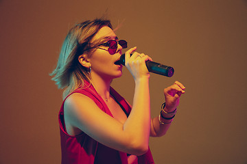 Image showing Young caucasian female musician, performer singing, dancing in neon light on gradient background