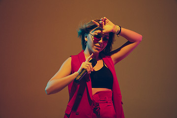 Image showing Young caucasian female musician, performer singing, dancing in neon light on gradient background