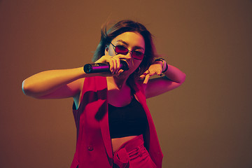 Image showing Young caucasian female musician, performer singing, dancing in neon light on gradient background