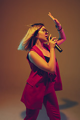 Image showing Young caucasian female musician, performer singing, dancing in neon light on gradient background