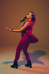 Image showing Young caucasian female musician, performer singing, dancing in neon light on gradient background