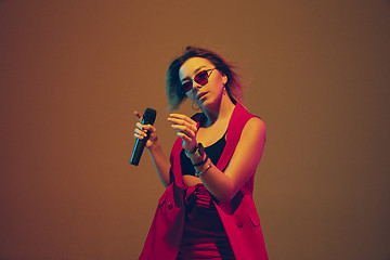 Image showing Young caucasian female musician, performer singing, dancing in neon light on gradient background