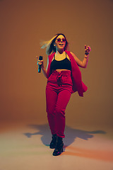 Image showing Young caucasian female musician, performer singing, dancing in neon light on gradient background