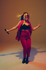 Image showing Young caucasian female musician, performer singing, dancing in neon light on gradient background