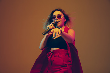 Image showing Young caucasian female musician, performer singing, dancing in neon light on gradient background