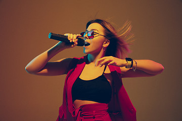 Image showing Young caucasian female musician, performer singing, dancing in neon light on gradient background