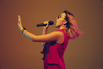 Image showing Young caucasian female musician, performer singing, dancing in neon light on gradient background