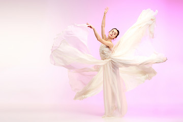 Image showing Ballerina. Young graceful female ballet dancer dancing over pink studio. Beauty of classic ballet.