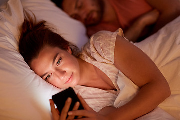 Image showing woman using smartphone while boyfriend is sleeping