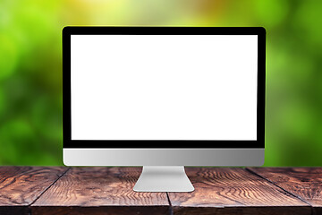 Image showing Mockup computer screen on wooden table against a blurred background.