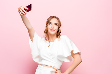 Image showing Portrait of a young attractive woman making selfie photo with smartphone on a pink background