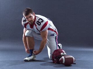 Image showing American Football Player tie his shoe laces isolated on gray