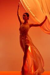 Image showing Ballerina. Young graceful female ballet dancer dancing over red studio. Beauty of classic ballet.