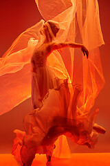 Image showing Ballerina. Young graceful female ballet dancer dancing over red studio. Beauty of classic ballet.