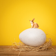 Image showing sweet Easter Bunny is sitting on a big egg yellow background