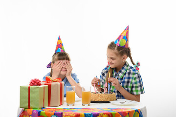 Image showing One girl covered her eyes with her hands, the other inserts matches in a birthday cake