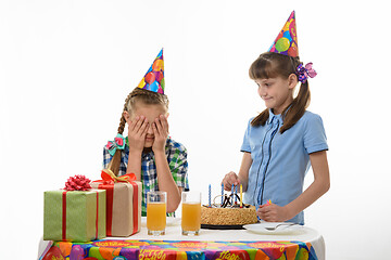 Image showing While one girl inserts candles in a birthday cake, another girl covers her face with her palms