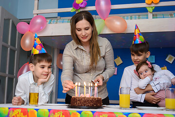 Image showing Mom lights candles at a birthday celebration in the children\'s room, around the children