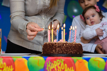 Image showing Mom lights candles on a cake at a birthday party