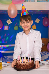 Image showing A boy at his birthday stands at the table with a cake
