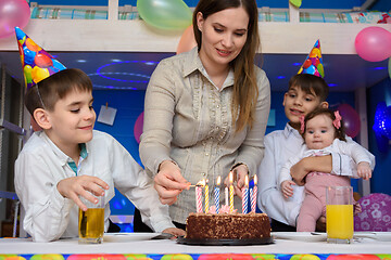 Image showing Girl lights candles on a pie at the festive table