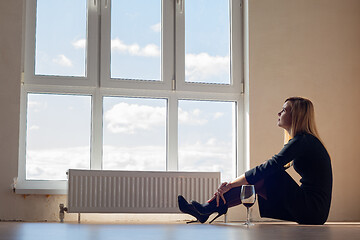 Image showing Sad girl sitting by the window in an empty apartment with a glas