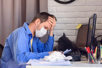 Image showing A man in a protective medical mask sits at a computer in a home stop and reads documents