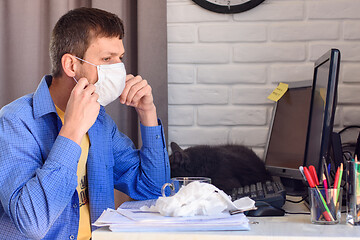 Image showing A man puts on a protective medical mask while working at home at the computer