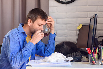 Image showing A sick man sits at a computer and drinks tea