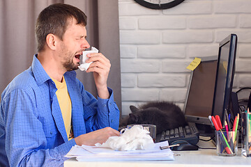 Image showing Young man sneezes while at a computer