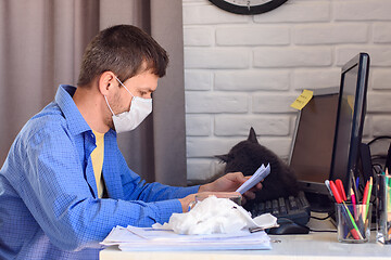 Image showing A man in a medical mask reads a document while working remotely