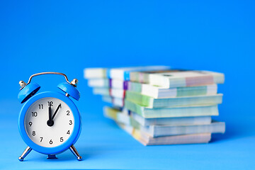 Image showing In the foreground is an alarm clock, in the background is a stack of bills