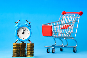 Image showing A clock stands on a stack of coins, in the background a grocery cart