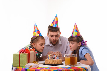 Image showing Dad and two daughters together blow out the candles on the cake