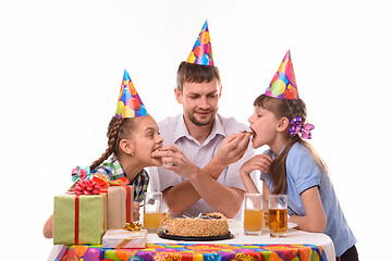 Image showing Kids bite pieces of cake from dad\'s hands, having fun celebrating a birthday