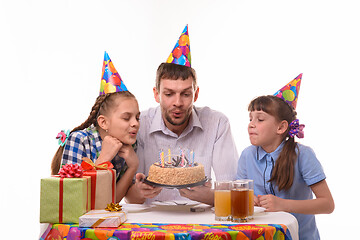 Image showing Father and two daughters blow out candles on a birthday cake