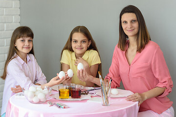 Image showing Mom and two daughters are sitting at the table preparing eggs for Easter and looked in the frame