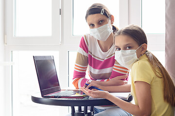 Image showing Mom and girl in self-isolation mode are sitting at the table, doing homework and looked into the frame.