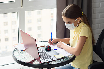 Image showing Girl in medical mask does homework using distance learning