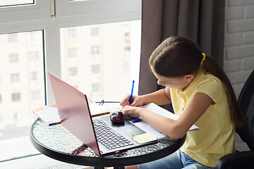 Image showing Girl doing homework in a room, sitting at a table by the window