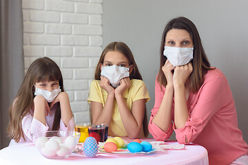 Image showing Mom and two daughters at the table in medical masks paint Easter eggs for the holiday