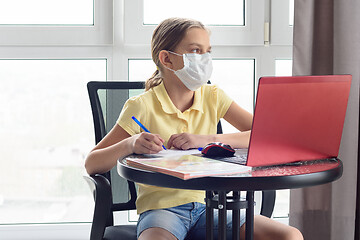 Image showing A girl in a medical mask on quarantine in isolation isolates herself remotely from her lessons and distracted, looked out the window