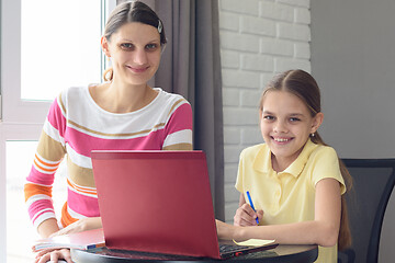 Image showing Happy girl and mom with a smile look at the frame, sitting at the table and doing homework