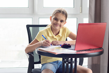 Image showing The girl at the table at home does homework and looked into the frame.