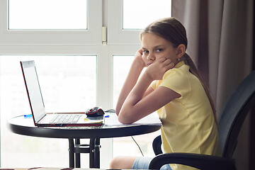 Image showing An upset girl sits at a table at home, does homework and looks with displeasure